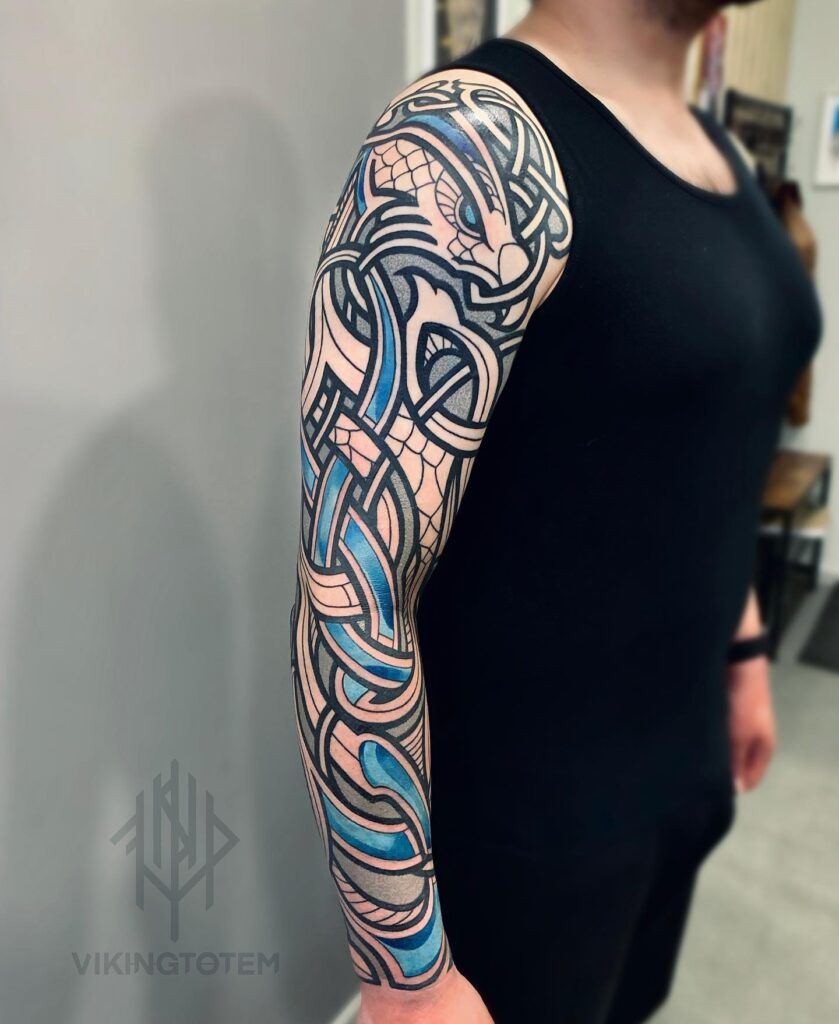 A full sleeve Viking-inspired tattoo with a serpent design in black, gray, and blue shades, showcasing traditional Norse knotwork.