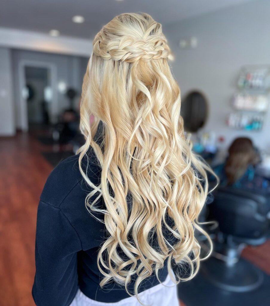 A woman’s back view showcasing a prom hairstyle with a waterfall braid merging into long, curled blonde hair, styled for a formal event.