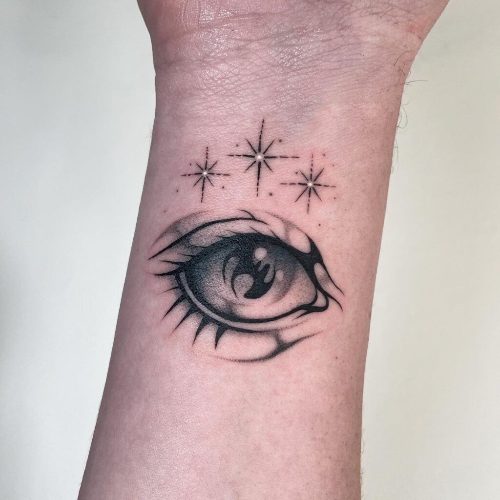 A black ink tattoo of an eye surrounded by starbursts on the wrist, symbolizing cosmic insight.