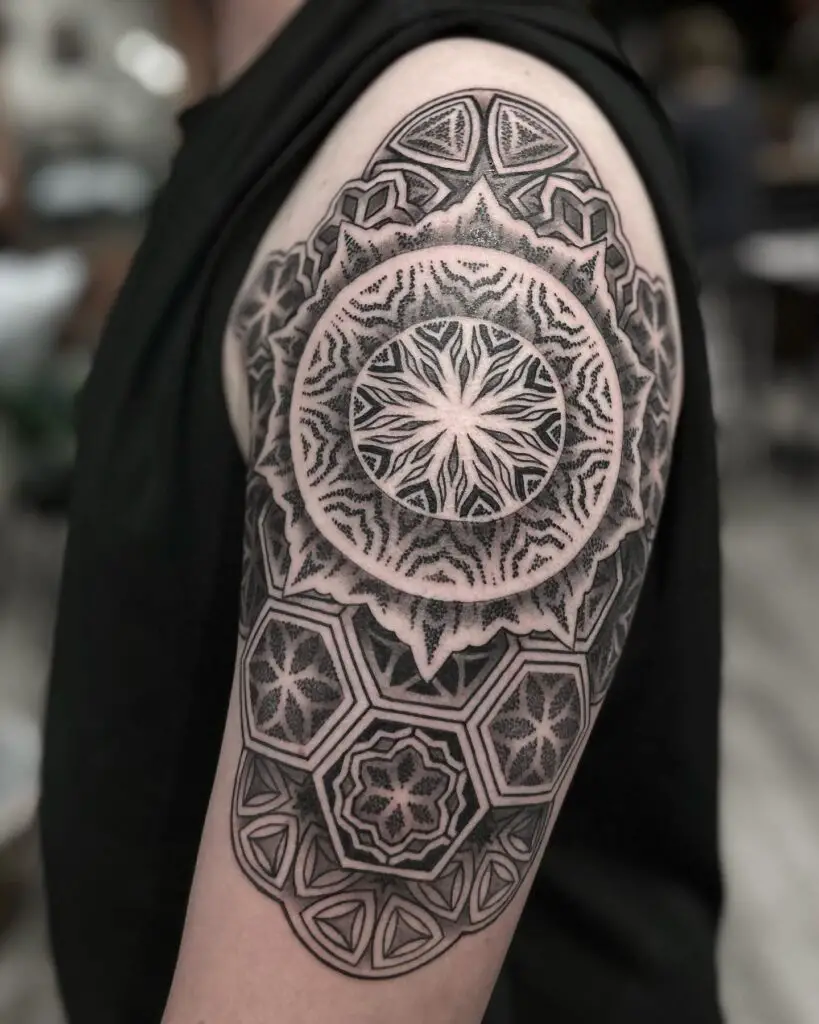 A shoulder cap tattoo with a central mandala design encircled by geometric patterns in a symmetrical layout.