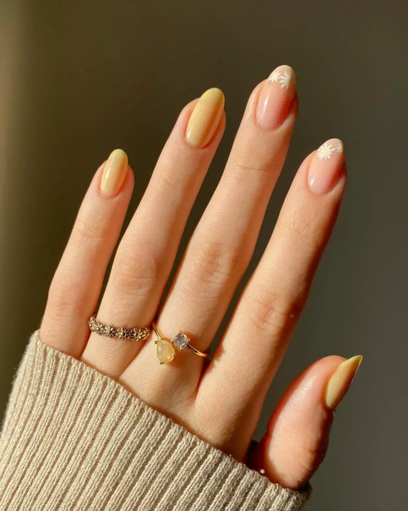 Ombre nails blending from yellow to peach with subtle daisy details, reminiscent of the peaceful colors of a sunset.
