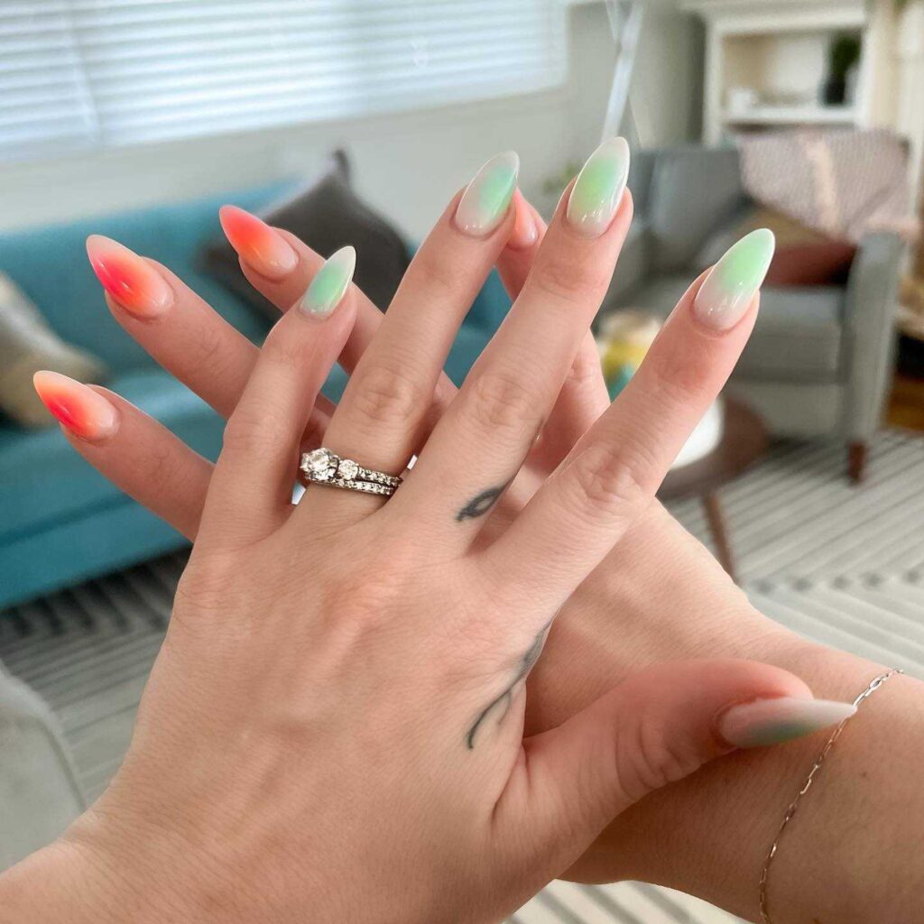 A hand with nails painted in a gradient from peach to mint green, evoking the colors of a spring sunrise.