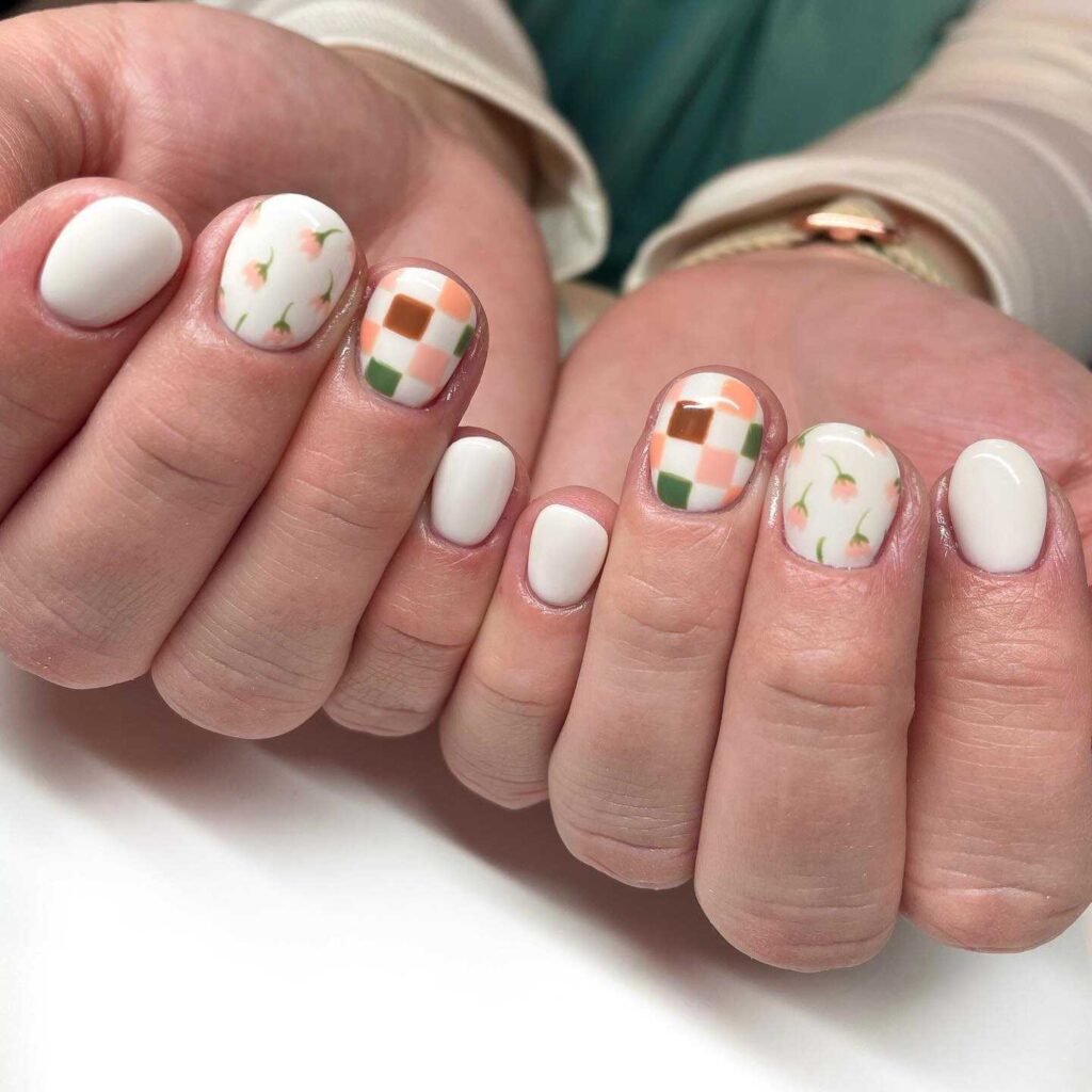 Rounded nails with a white base featuring modern geometric and floral designs in green and orange.