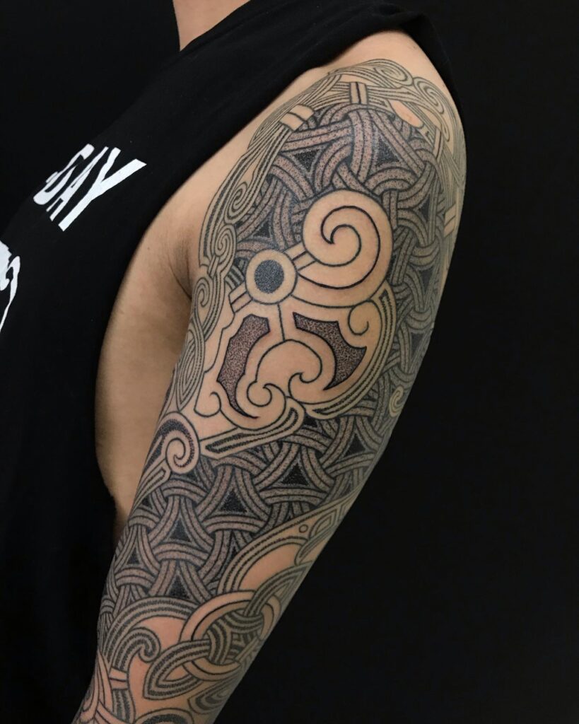 An arm tattoo of a Viking Sunwheel surrounded by knotwork with detailed shading for a 3D effect.