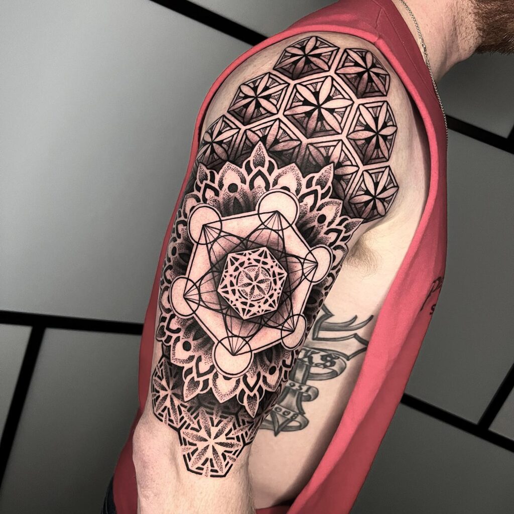 An arm tattoo with a dynamic geometric mandala design incorporating sharp lines and smooth curves in black ink.