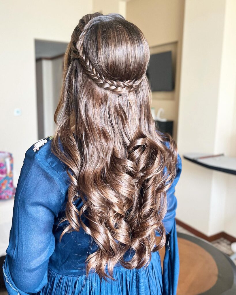 A brunette half-up hairstyle with a braided crown and soft curls, ideal for an elegant prom look.