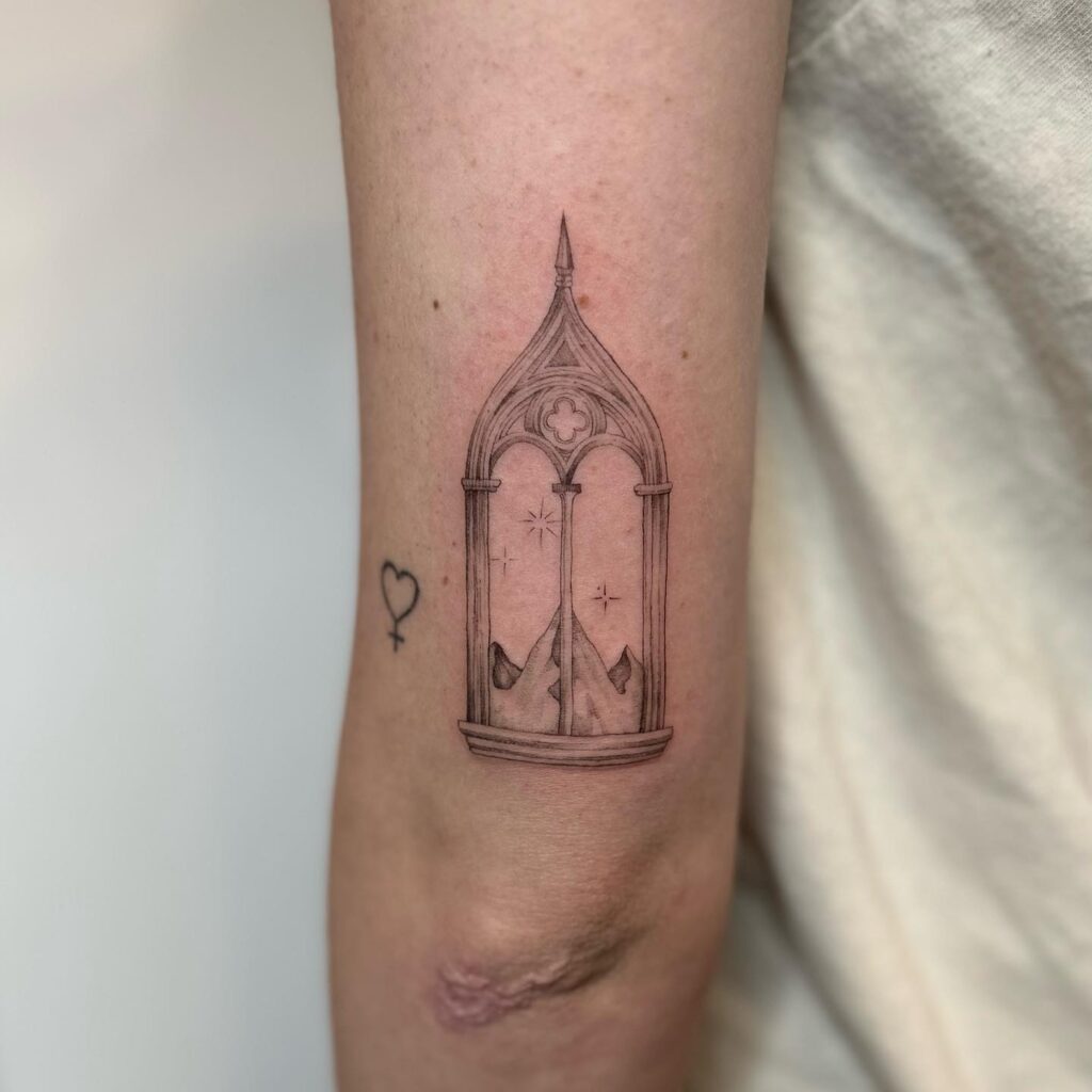 A gothic archway with a sword inside and stars around it, tattooed on an arm, symbolizing protected strength.