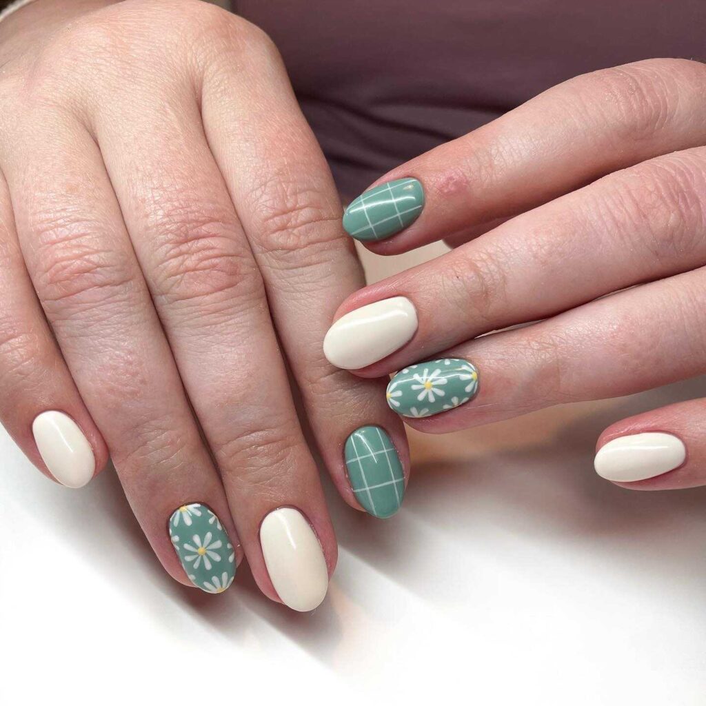 Nails painted with a serene sage green and creamy white, featuring daisy motifs and grid patterns, reflecting a garden-inspired aesthetic.