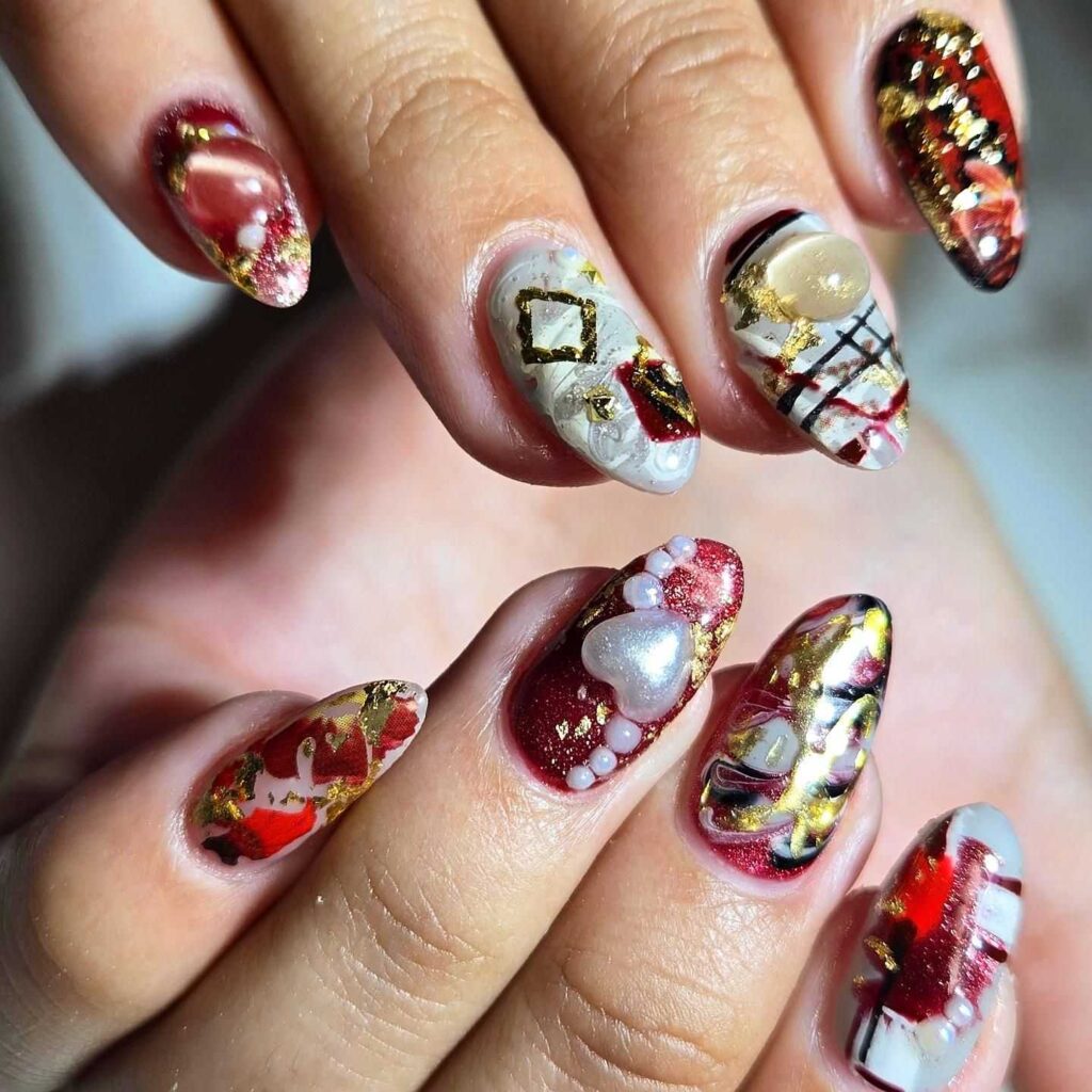 A hand showcasing nails with a lavish combination of red and gold accents, invoking the grandeur of a baroque aesthetic.