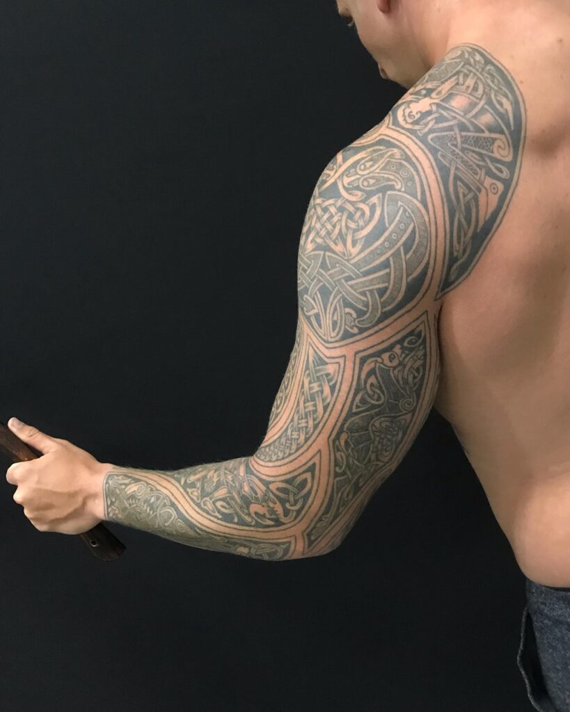 A full sleeve tattoo with a Norse beast and intricate knotwork in a muted color palette, evoking mythology.