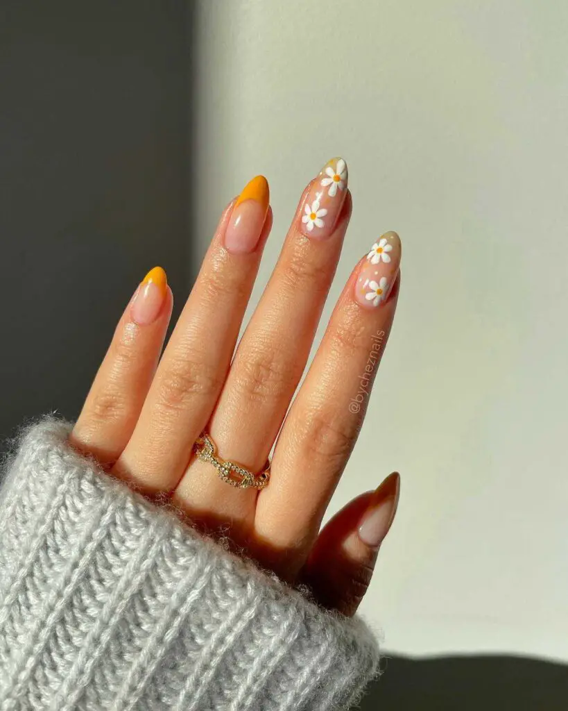 A hand with nails adorned in sunny yellow tips and pastel daisy accents, giving off a cheerful spring vibe.