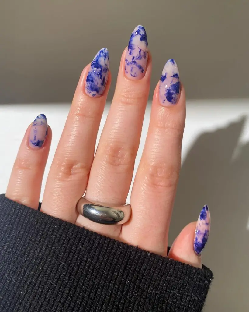 Fingers featuring a blue and white marbled nail design, reminiscent of ink strokes or natural stone patterns.