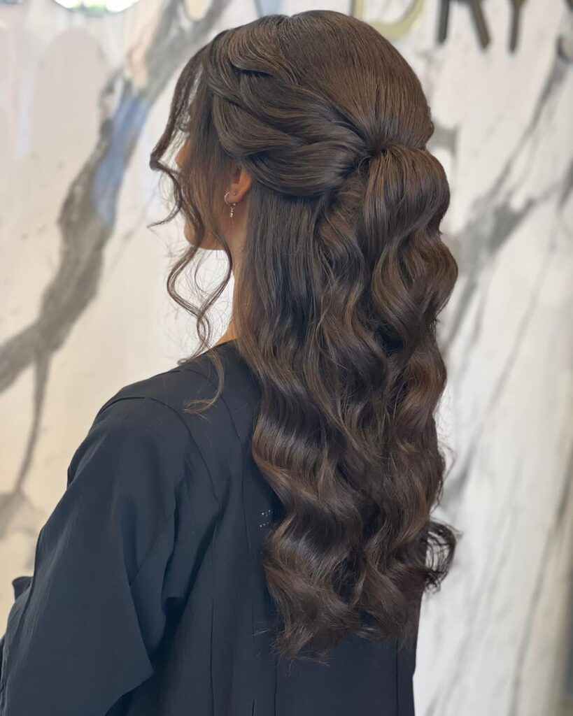 A side view of a brunette hairstyle featuring a side braid and flowing waves, styled for a sophisticated prom night.