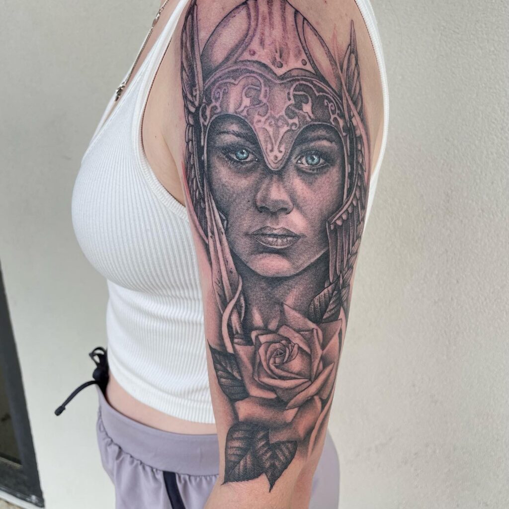 A detailed arm tattoo of a Valkyrie with a focused gaze, complete with Norse helmet and a rose.