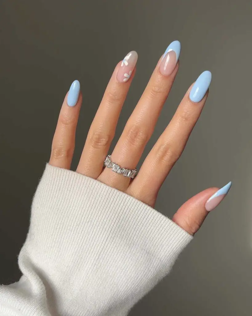 A hand with a white sweater sleeve, displaying nails with a sky blue base and cloud-like white patterns.