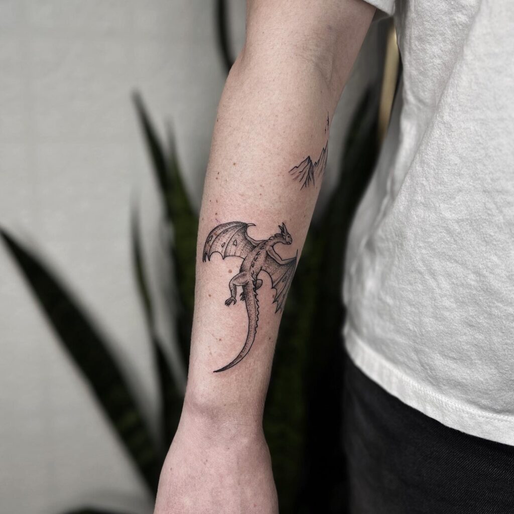 A detailed arm tattoo of a winged dragon in flight, representing freedom and mythological power.