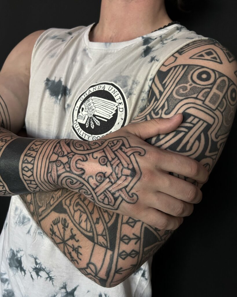 A full sleeve tattoo weaving Norse symbols like Thor's hammer and Odin's ravens with bold lines.