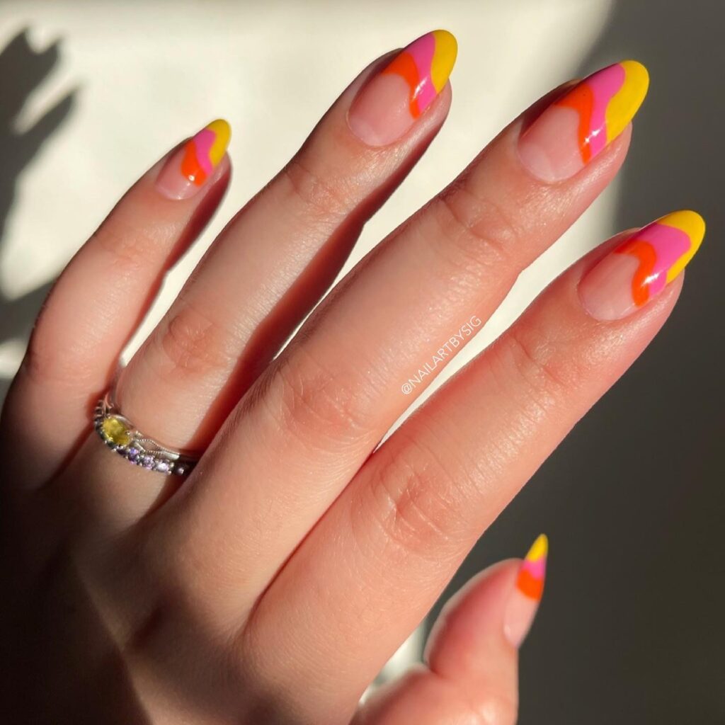A hand featuring playful swirls of sunset-inspired nail art in yellow, orange, and pink on a sheer nail base.