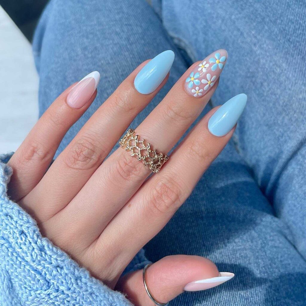 A hand with a blue denim sleeve reveals nails painted with soft blue and adorned with delicate white floral patterns.