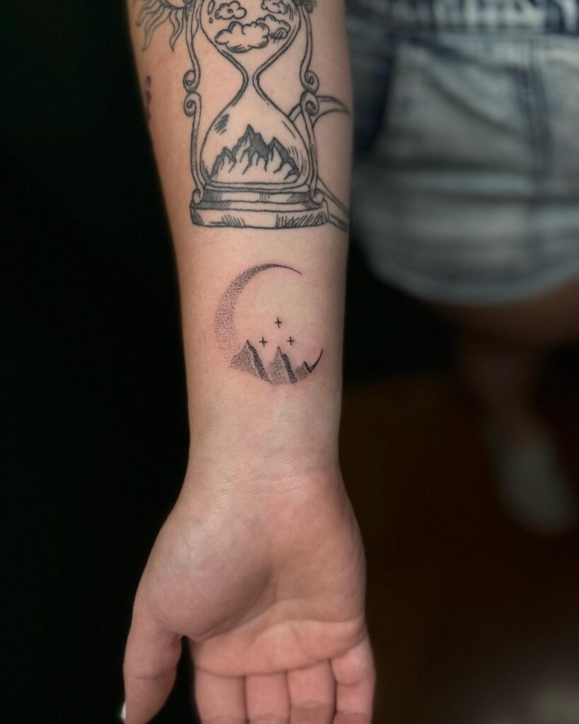 A tattoo on the wrist of a crescent moon with stars and mountains, representing serenity and guidance.