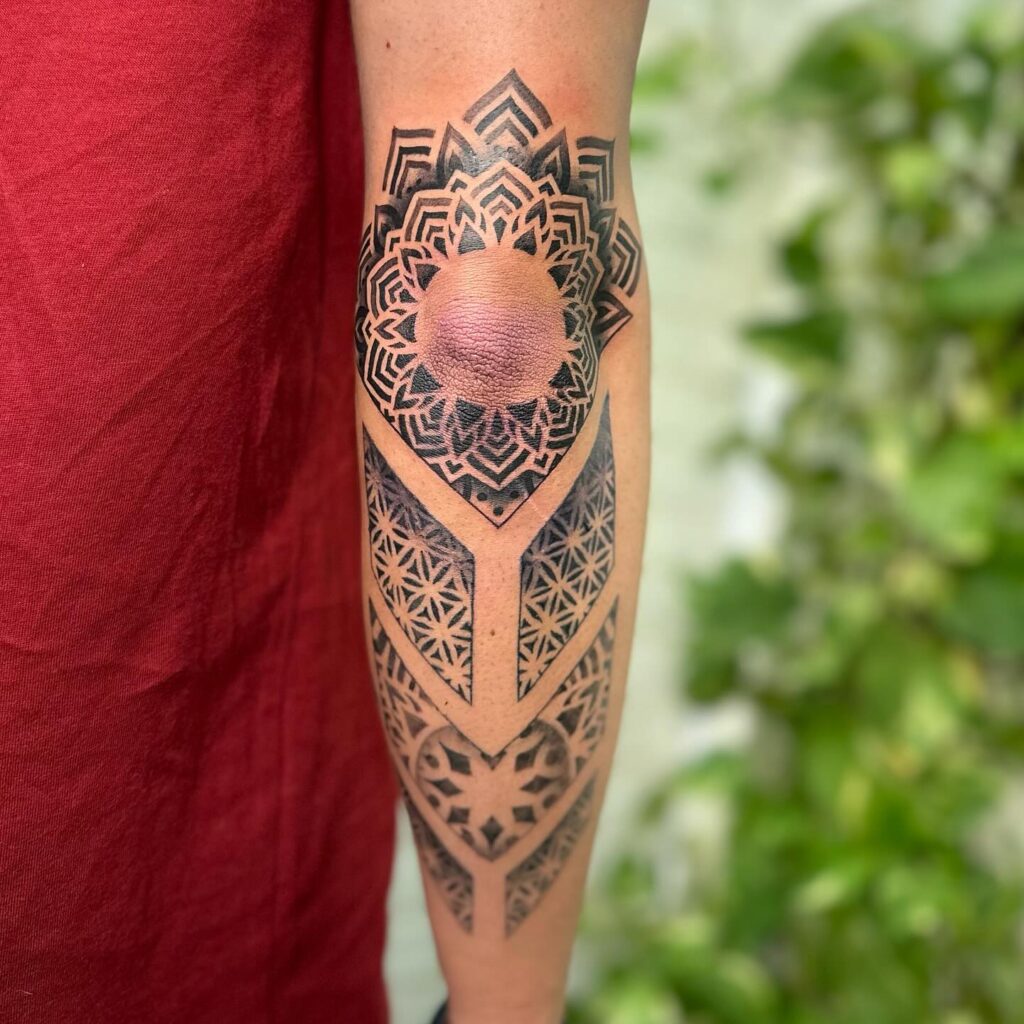 Arm tattoo with a central spherical mandala surrounded by detailed geometric patterns.