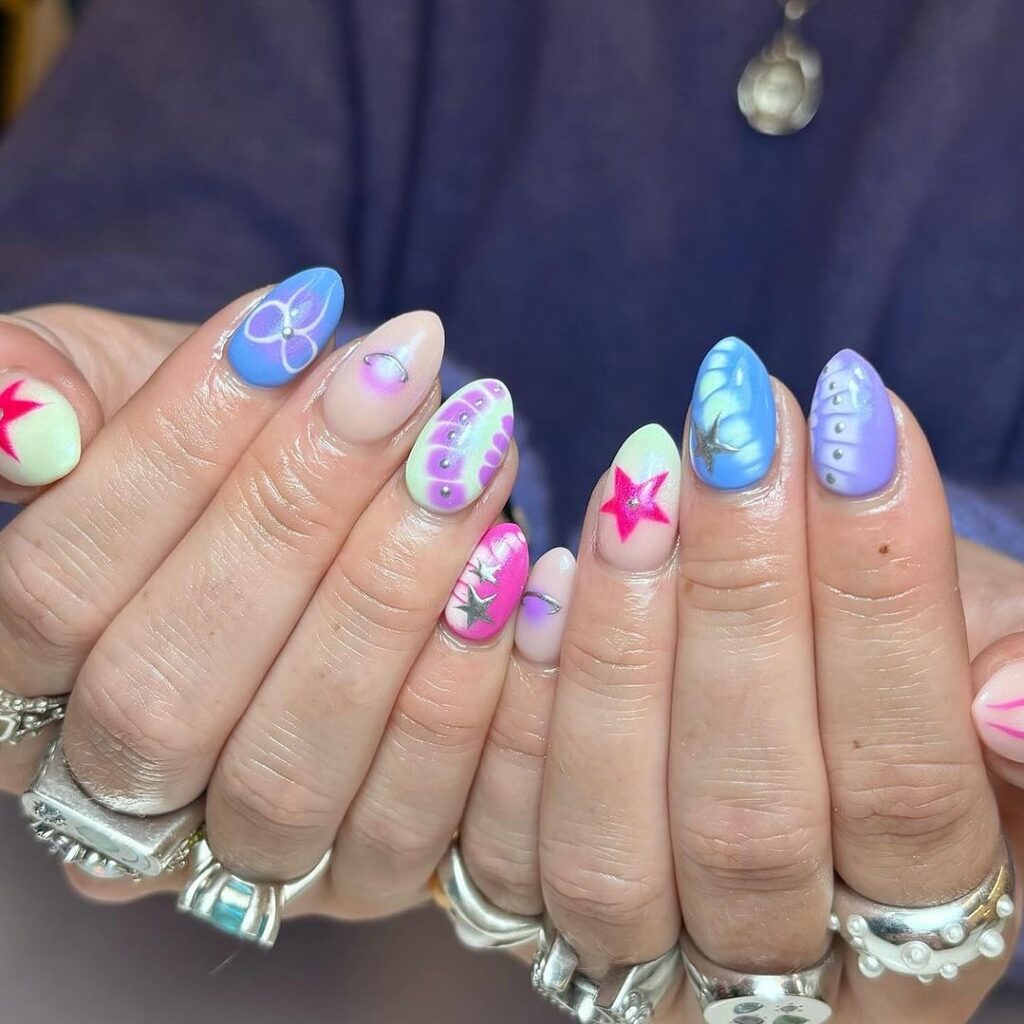 A hand adorned with nails painted in a variety of spring-inspired designs, featuring florals, pastels, and soft geometric patterns.