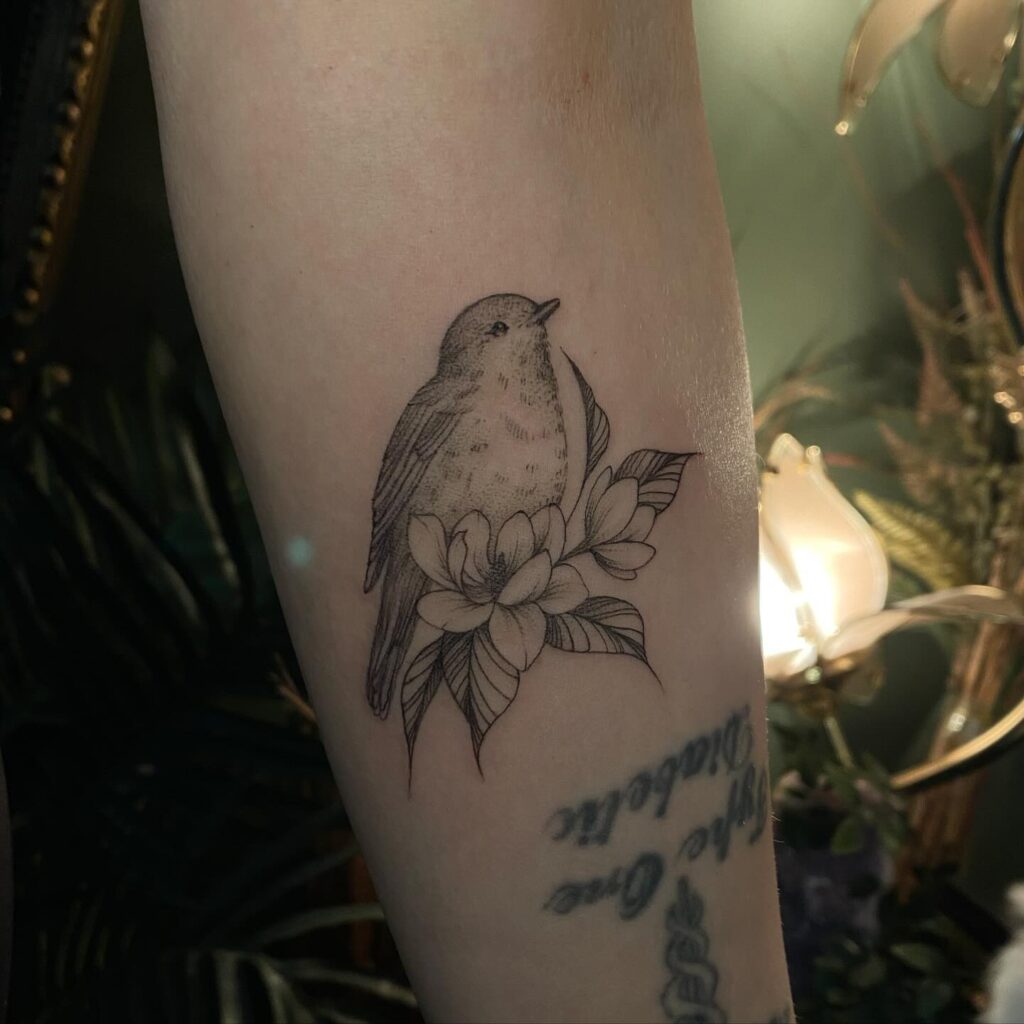 An arm tattoo featuring a bird among flowers, symbolizing freedom and the beauty of renewal.