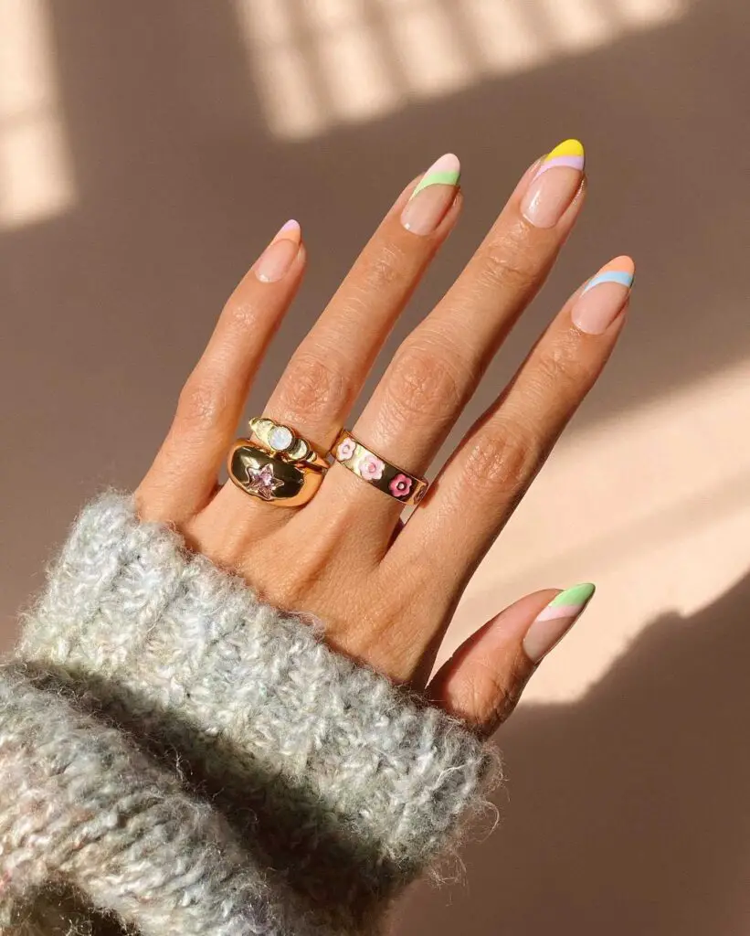 A hand emerging from a cozy knitted sweater cuff displays a minimalist nail design with pastel-colored tips.