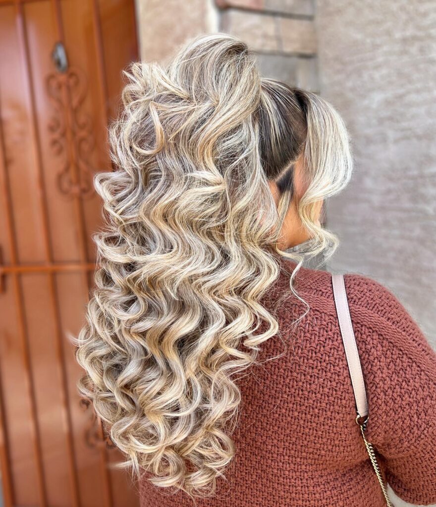 Woman with a luxurious balayage hairstyle, showcasing dark roots and blonde curls, perfect for a stylish prom look.