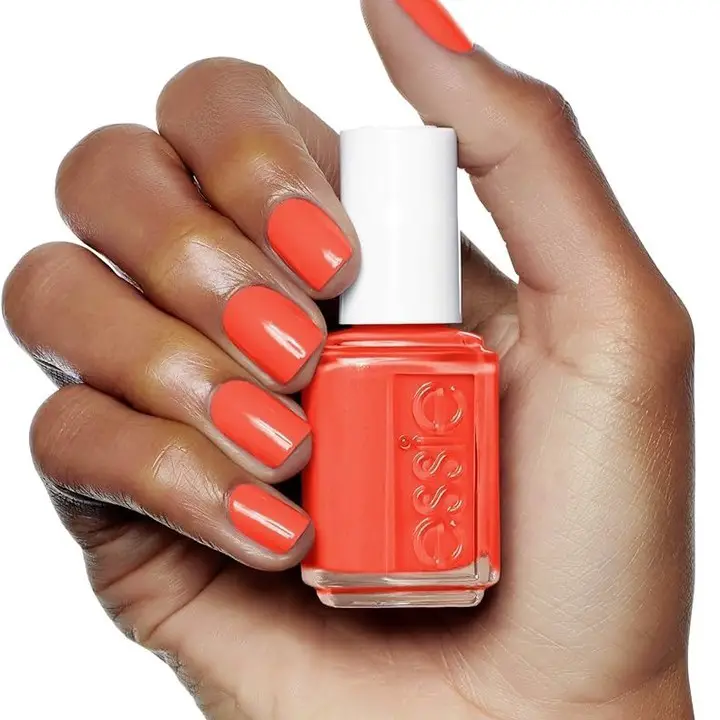 A hand holding a bottle of bright tangerine nail polish, with the nails painted in the same vivid color for a cheerful and energetic look.