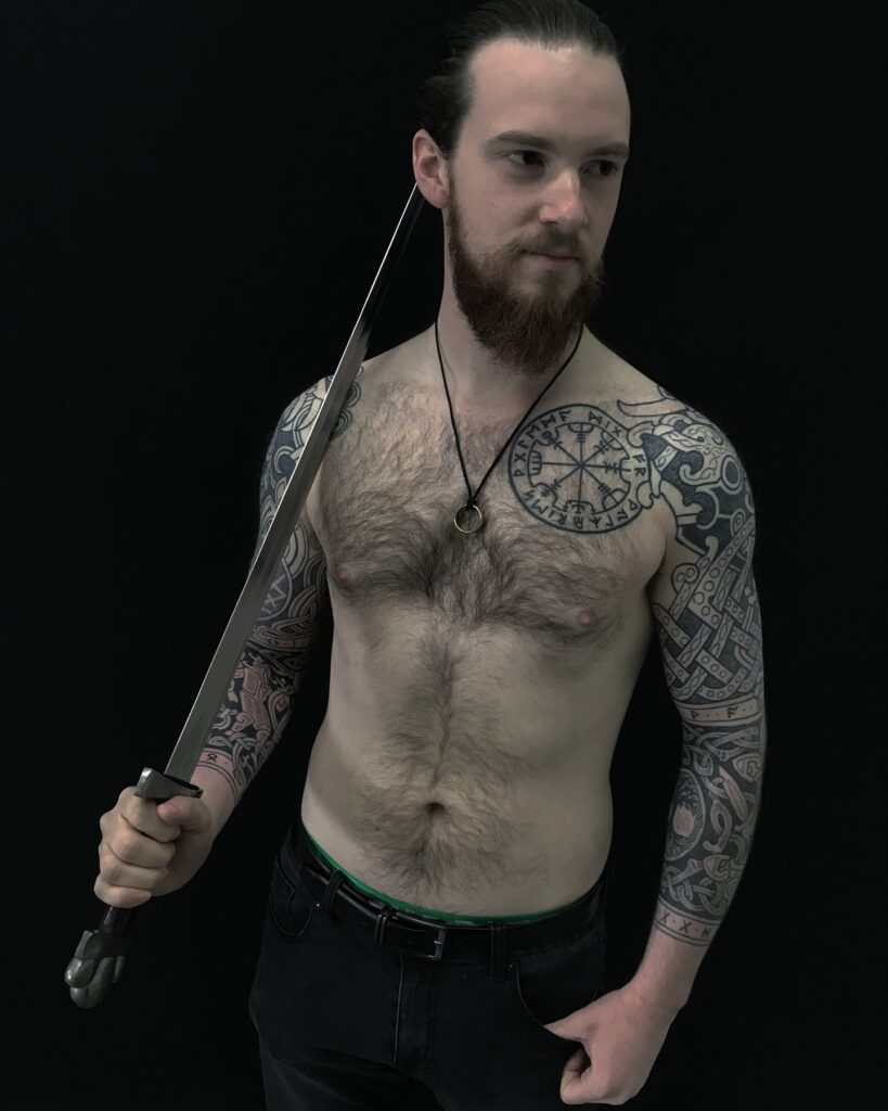 A man with a chest tattoo of the Vegvísir, surrounded by intricate Norse patterns.