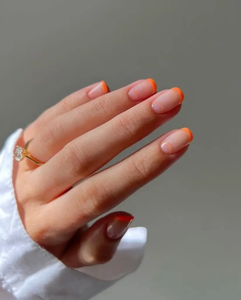 Elegant hand with a modern French manicure featuring a semi-translucent base and warm orange tips, accented by a delicate ring.