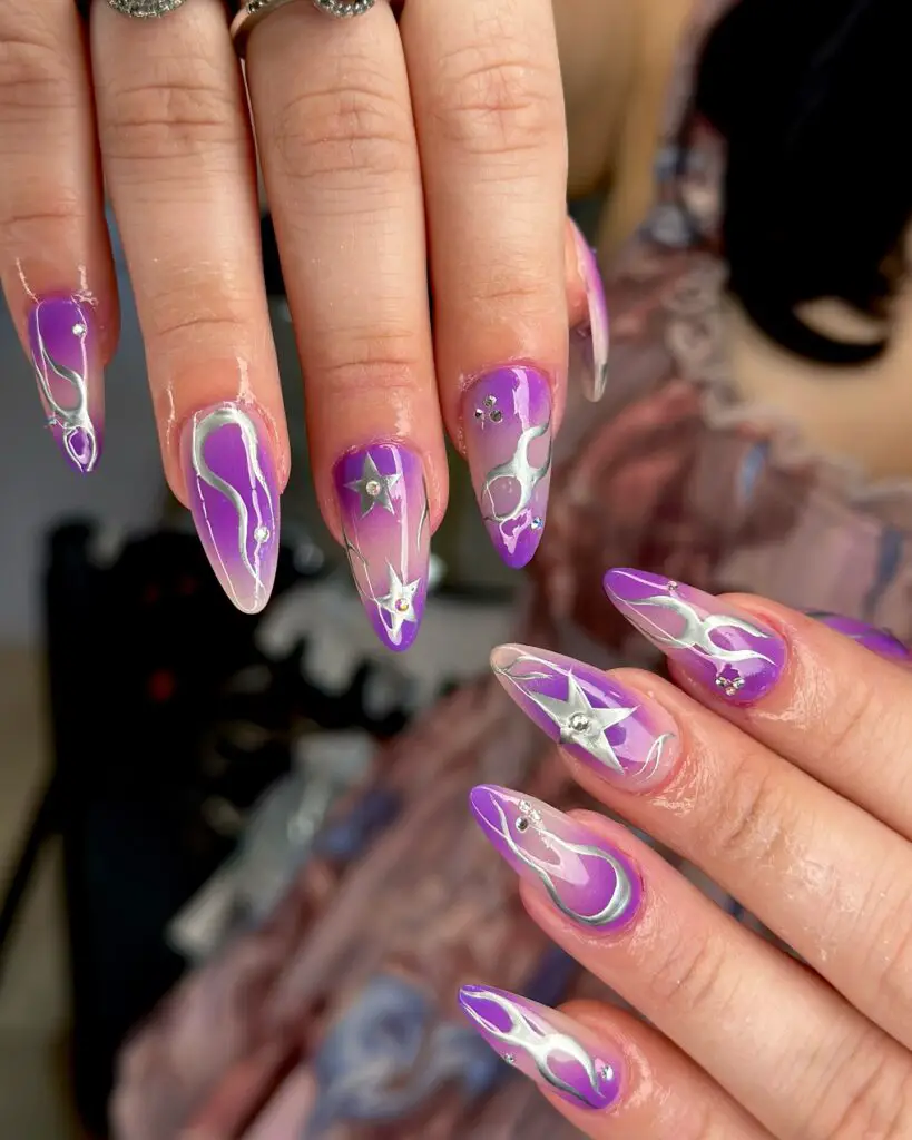 Nails with an artistic design of white and lavender swirls on a clear base, sprinkled with small star decorations.