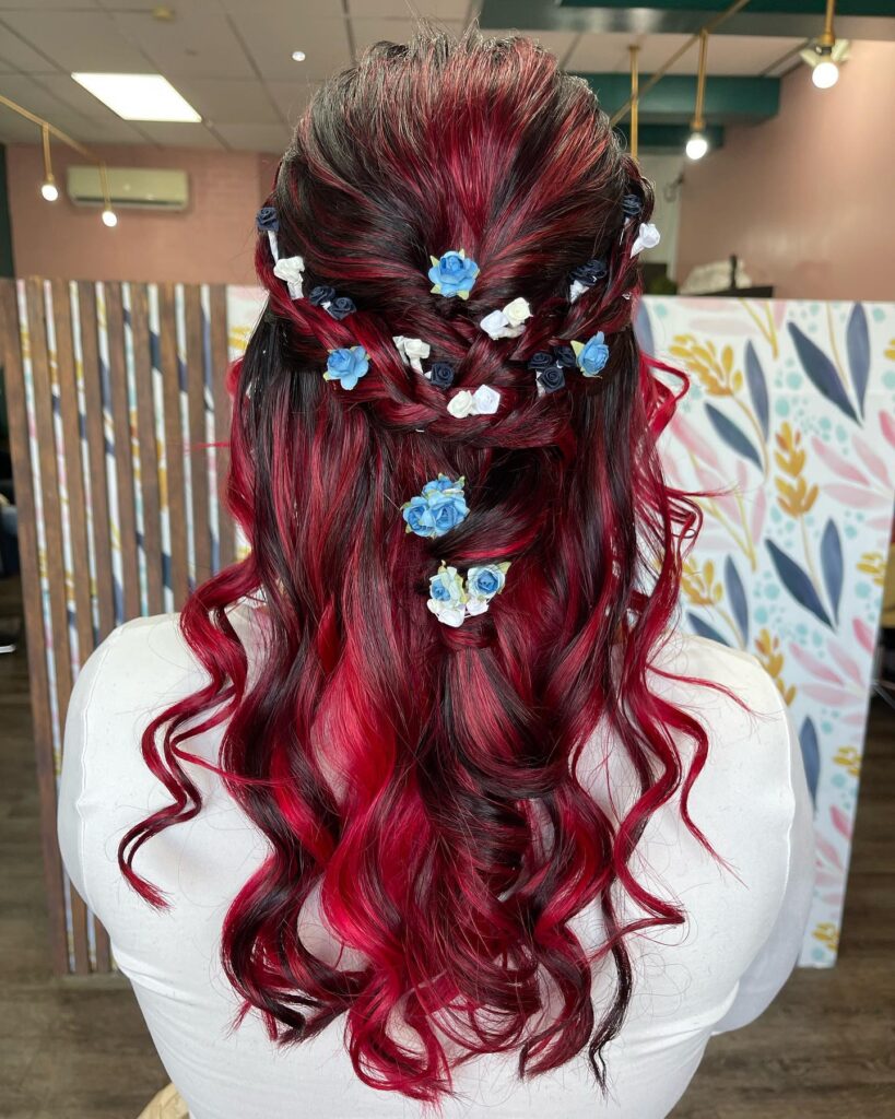 Red hair styled with a loose braid and blue floral accents, creating a bold and vibrant prom hairstyle.