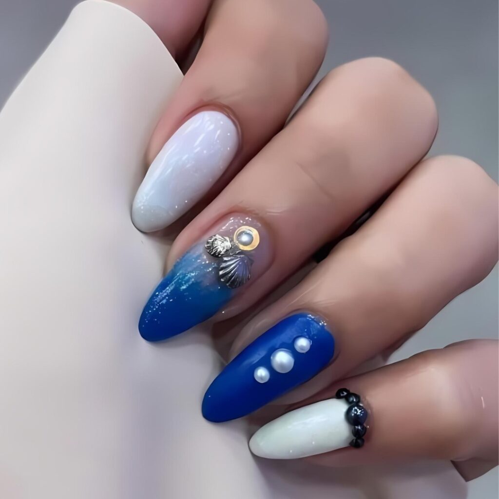 A hand showing off nails with an oceanic theme, including a deep blue gradient, pearl decorations, and a delicate seashell charm, evoking the elegance of the sea.