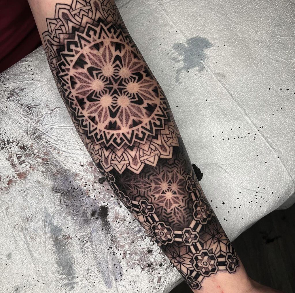 A detailed full-leg tattoo with black ink, consisting of symmetric mandala patterns with 3D effects.
