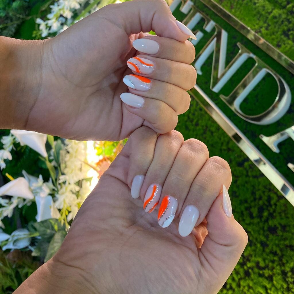 Bold coral streaks enhancing traditional French manicured tips on a background of sheer polish, offering a modern twist on a classic nail style.