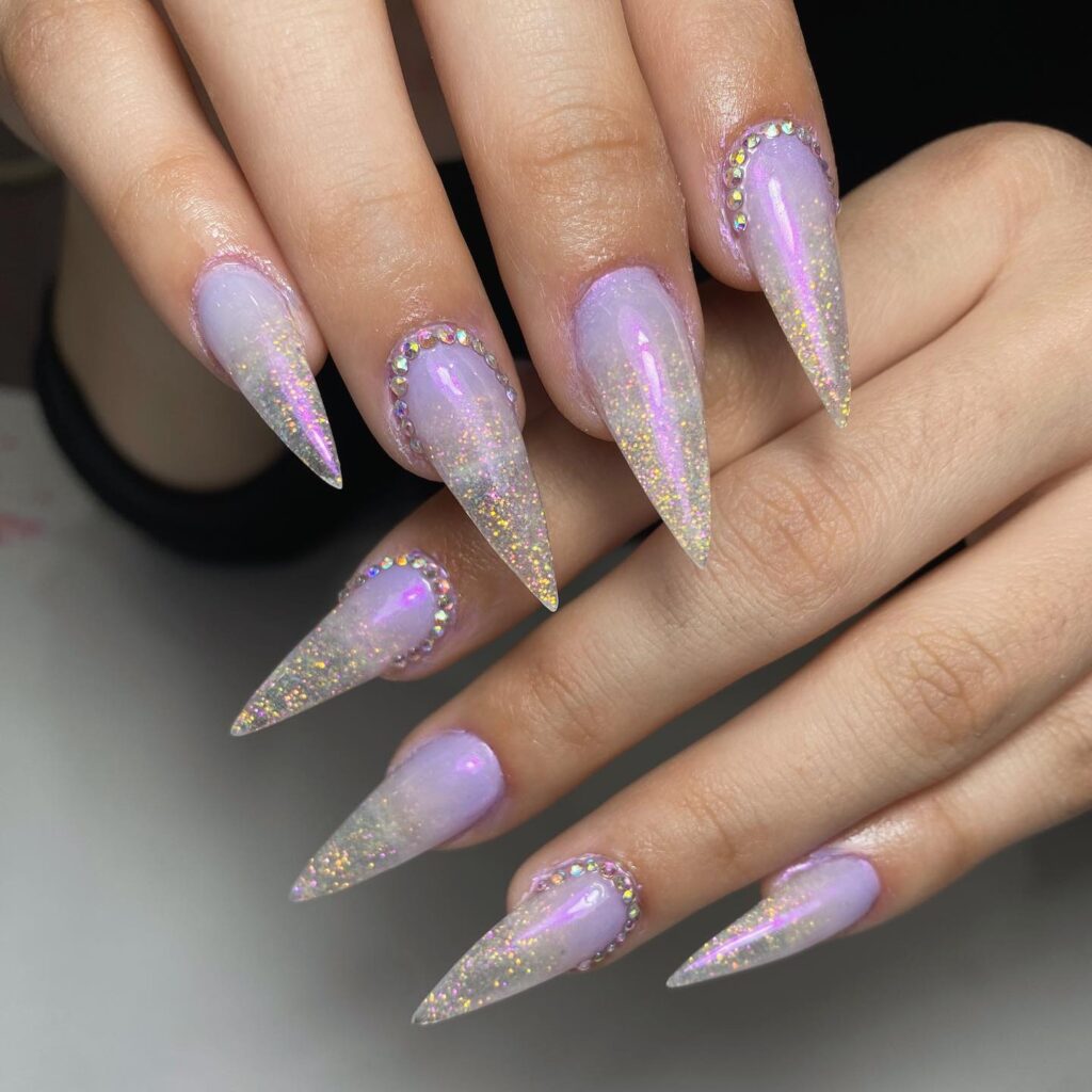 Stunning stiletto nails with a lavender glitter gradient and rhinestone embellishments, showcasing a dramatic and trendy spring nail design option.