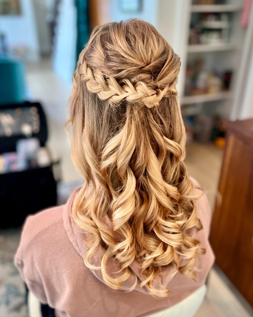 A close-up view of a woman's hairstyle with a braided crown and voluminous tousled curls, designed for a stylish and elegant prom look.