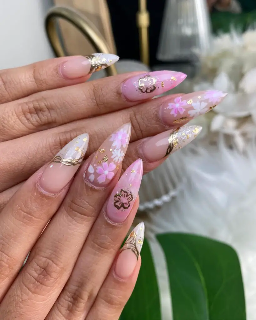 Almond-shaped nails painted with a Sakura blossom design in soft pinks and whites, accented with gold flakes for an elegant spring look.