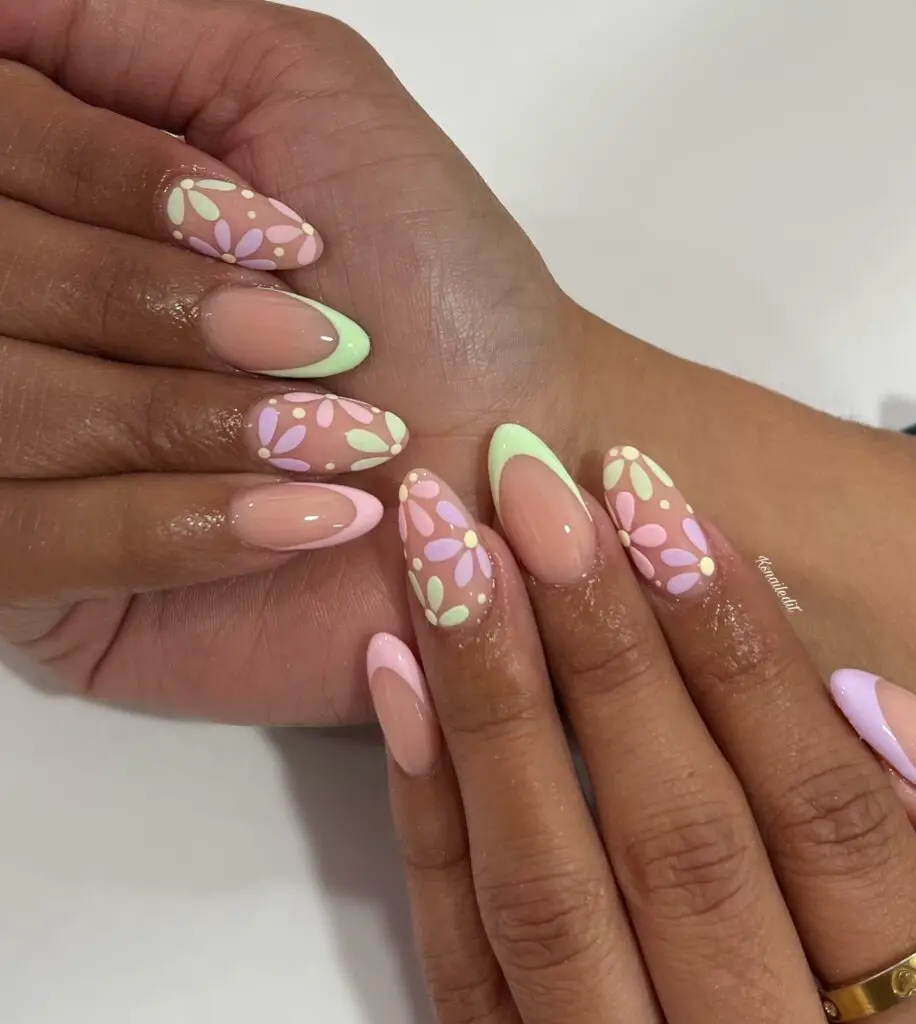 Hands with nails painted in a pastel pink base featuring green petal tips and delicate white floral accents, creating a spring garden feel.