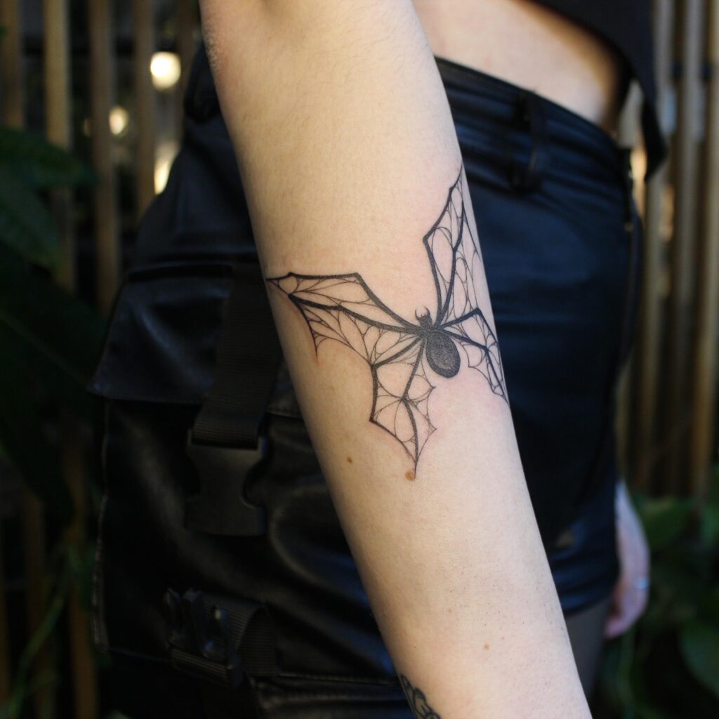 An arm tattoo of a detailed spider web with a spider, symbolizing life's complexity and creativity.