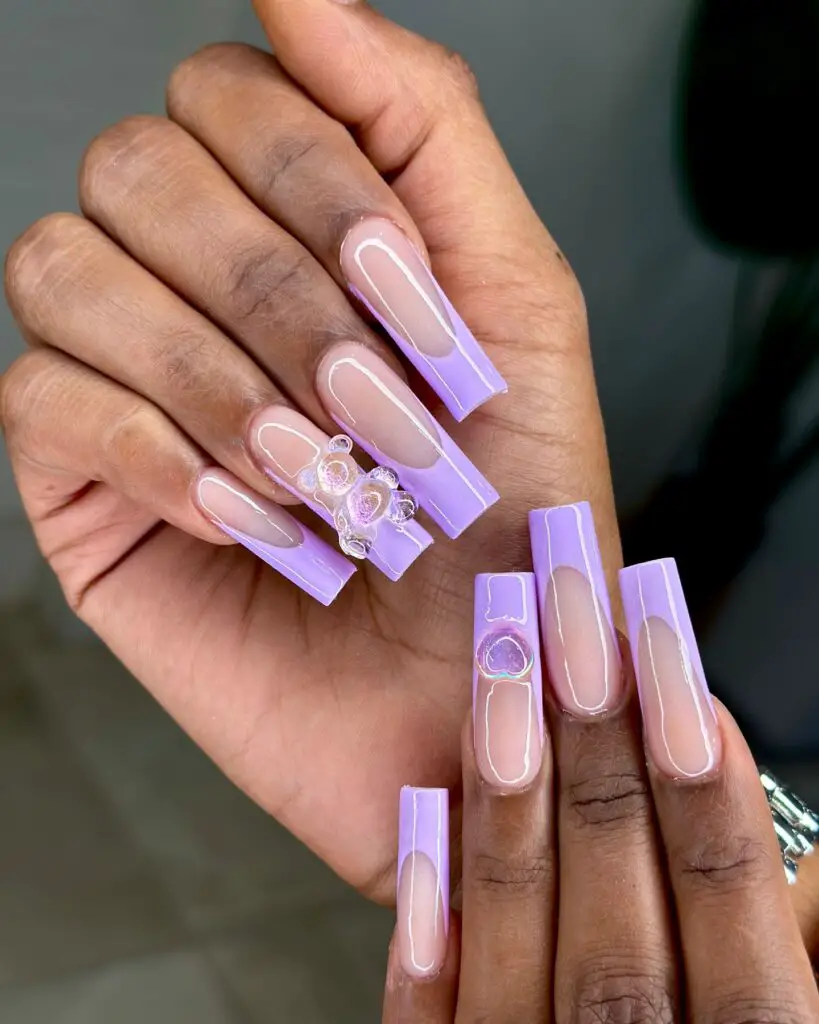 A hand displaying nails with a clear polish, outlined in lavender, and one accent nail with three-dimensional circular embellishments.