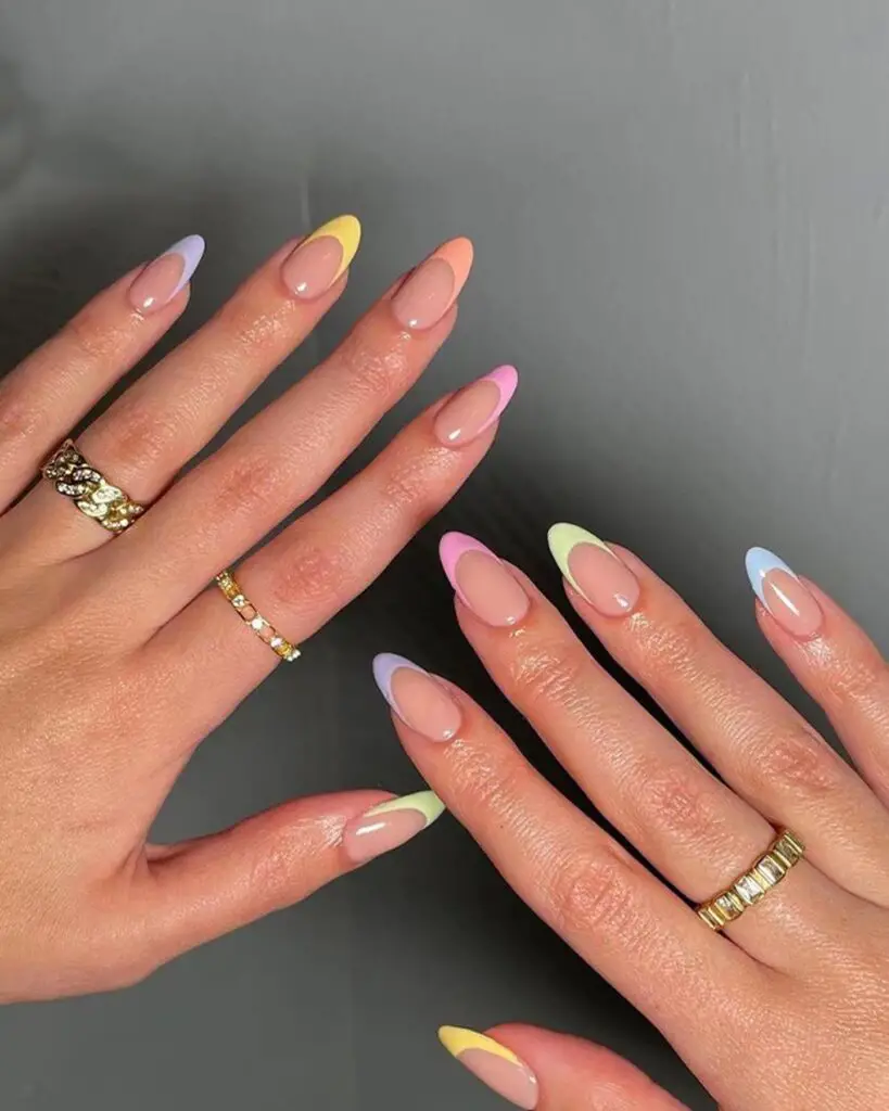 Elegant hands adorned with soft pastel ombre tips in shades of purple, pink, yellow, and blue on a natural nail base, enhanced by luxurious gold rings.