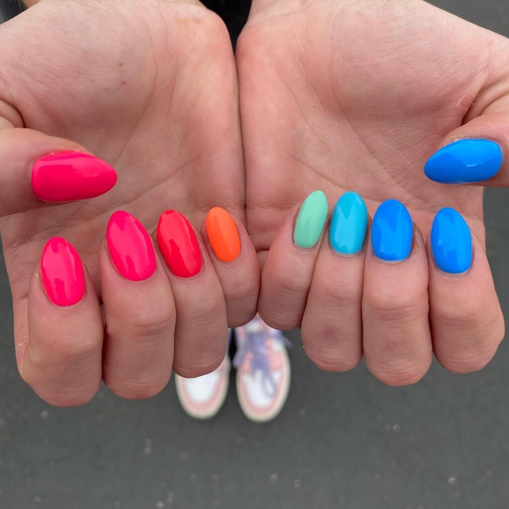 Two hands showing a vibrant selection of bright, solid-colored nails ranging from hot pink to sky blue.