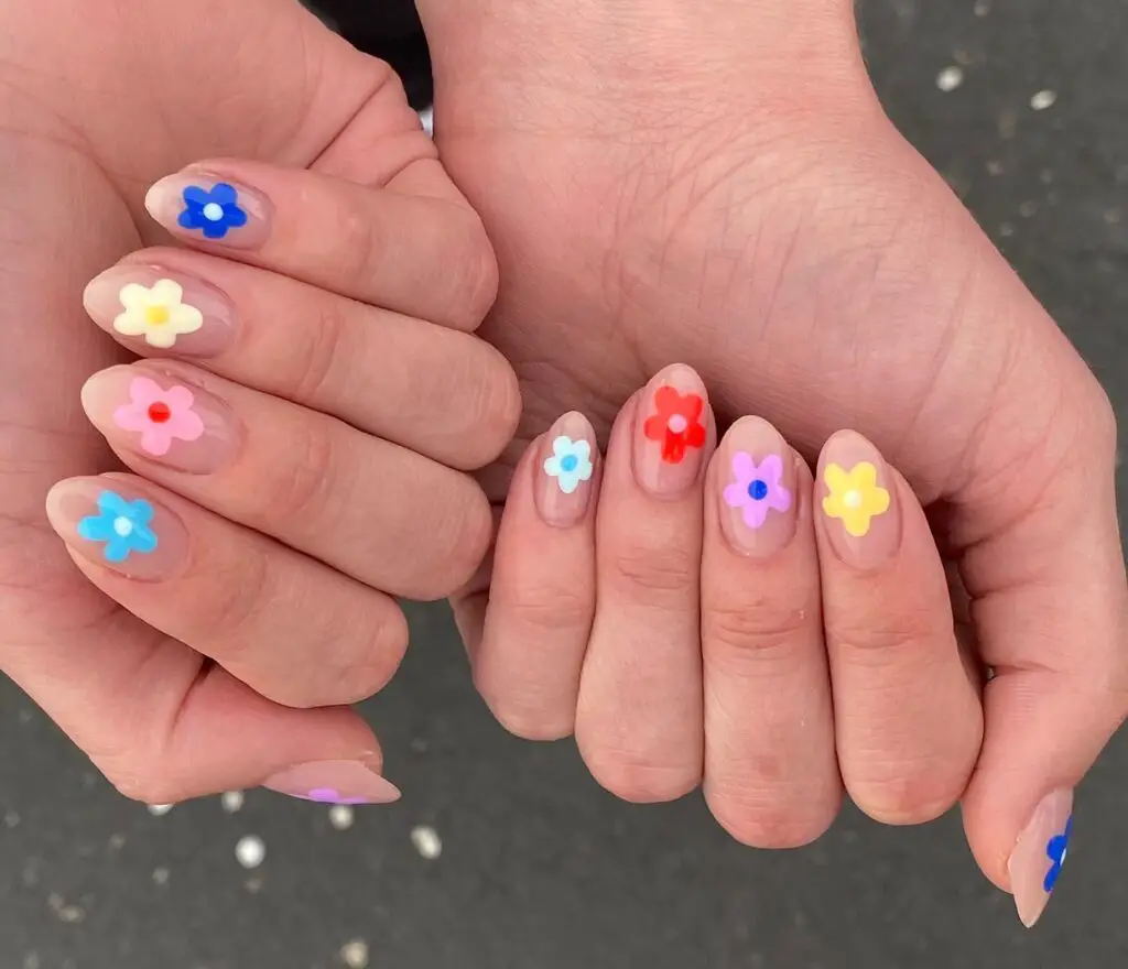 Hands cupped together, displaying nails with sheer bases adorned with small, colorful flower designs in a variety of hues.