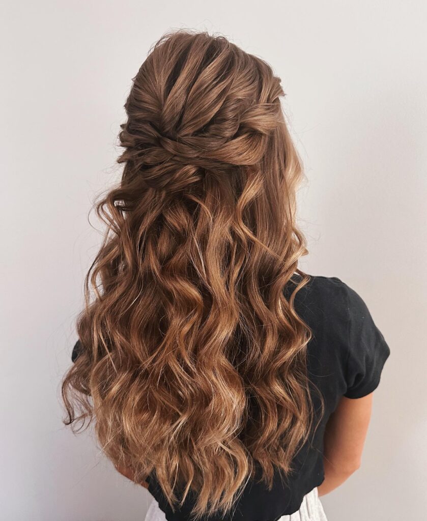 A woman's half-up hairstyle with a braided crown and long, flowing curls, styled for prom night elegance.