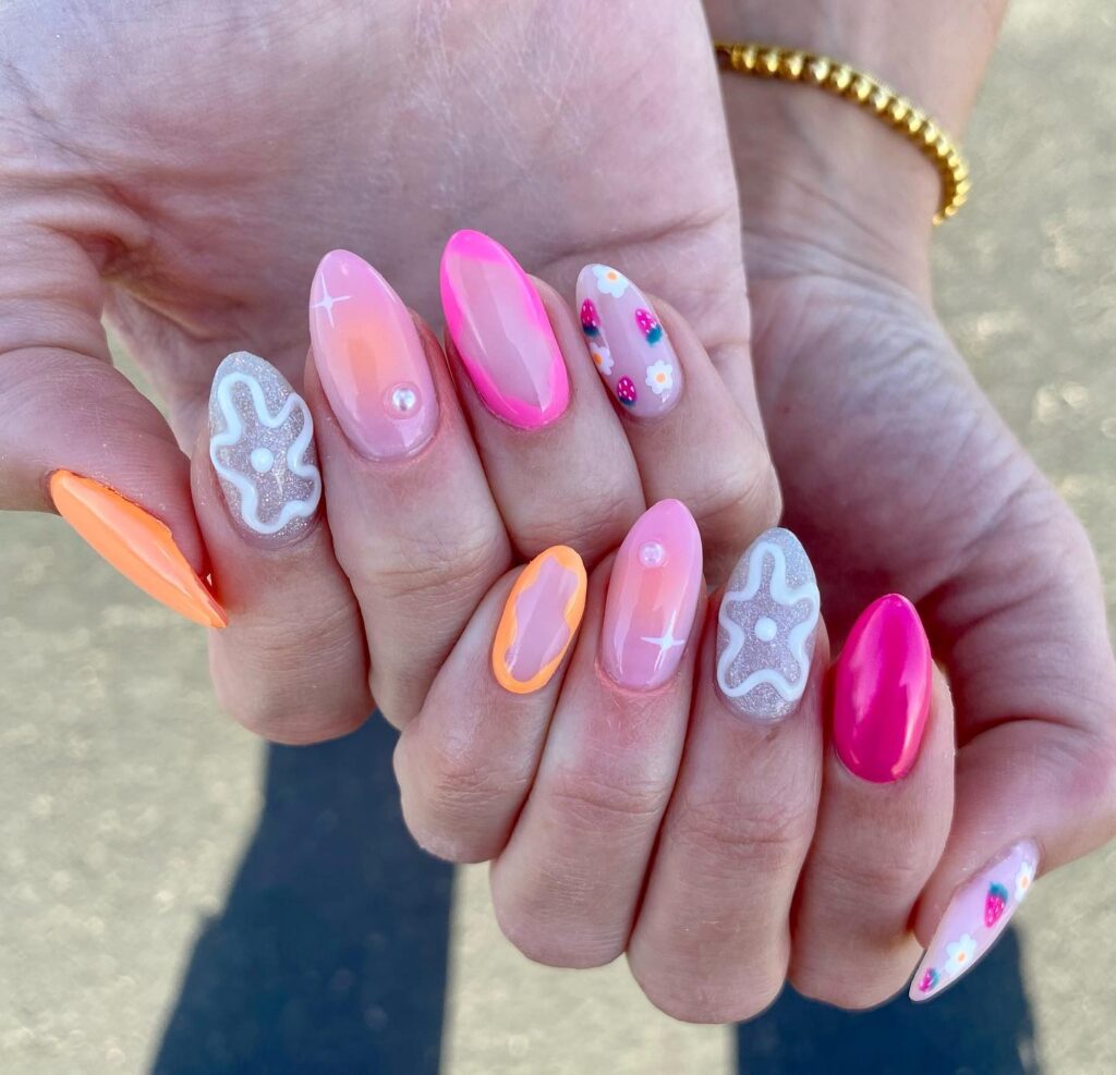 Hands showcasing a variety of spring-inspired nail designs with pastel pink and vibrant orange hues, floral patterns, and sparkling accents.
