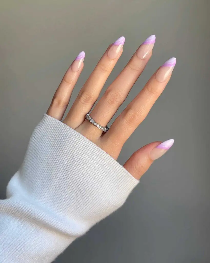 A hand displaying stiletto-shaped nails with a lavender French tip design, showcasing a modern take on classic elegance suitable for spring fashion.