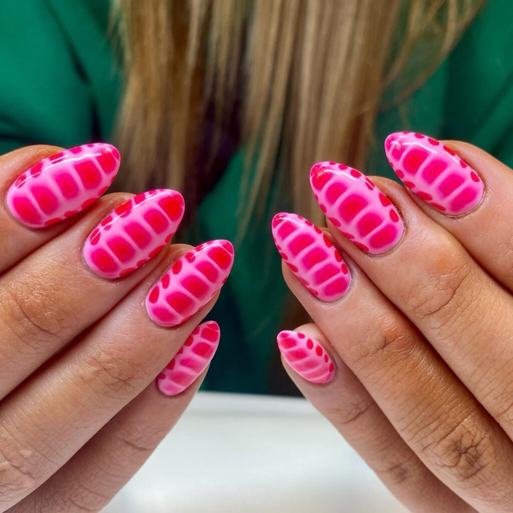 Hands showing almond-shaped nails with a bright pink base and raised pink grid-like texture, contrasted with a green background.